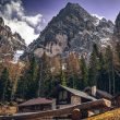 A scenic view of mountain cabins surrounded by towering mountains and trees under a cloudy sky.