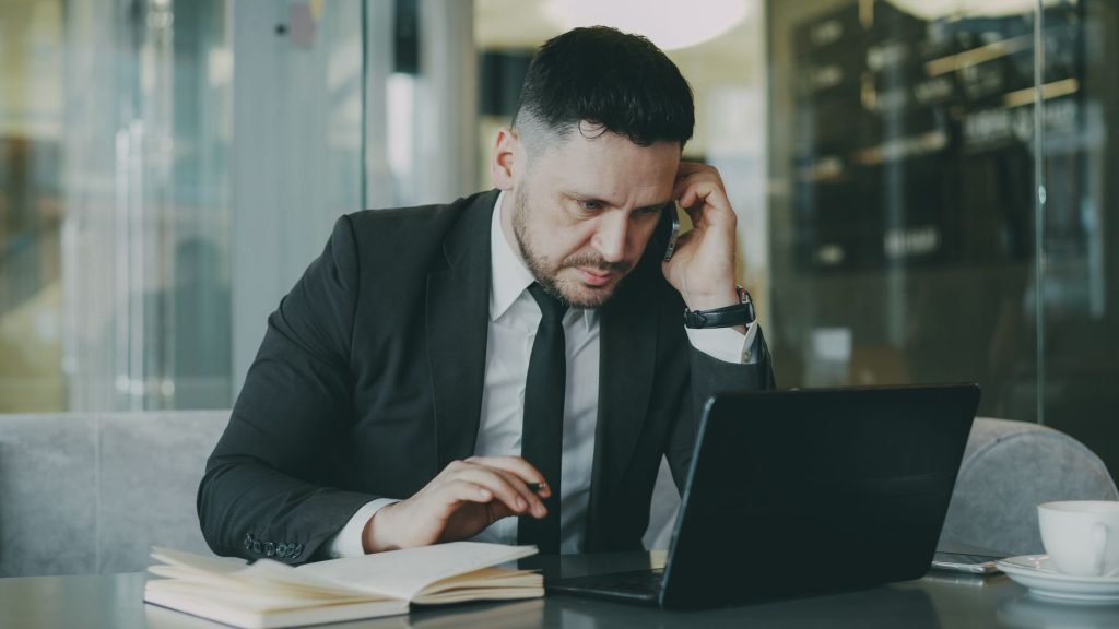 Focused businessman in suit multitasking on phone and laptop in modern office. — How MT4 for iOS Delivers Real-Time Market Ac