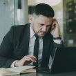 Focused businessman in suit multitasking on phone and laptop in modern office. — How MT4 for iOS Delivers Real-Time Market Ac