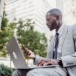 Businessman in a suit using a laptop and smartphone in an urban setting, blending technology with business. — Managing Forex