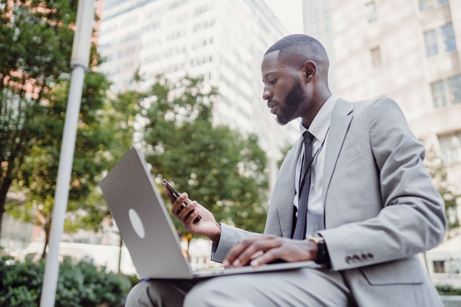 Businessman in a suit using a laptop and smartphone in an urban setting, blending technology with business. — Managing Forex