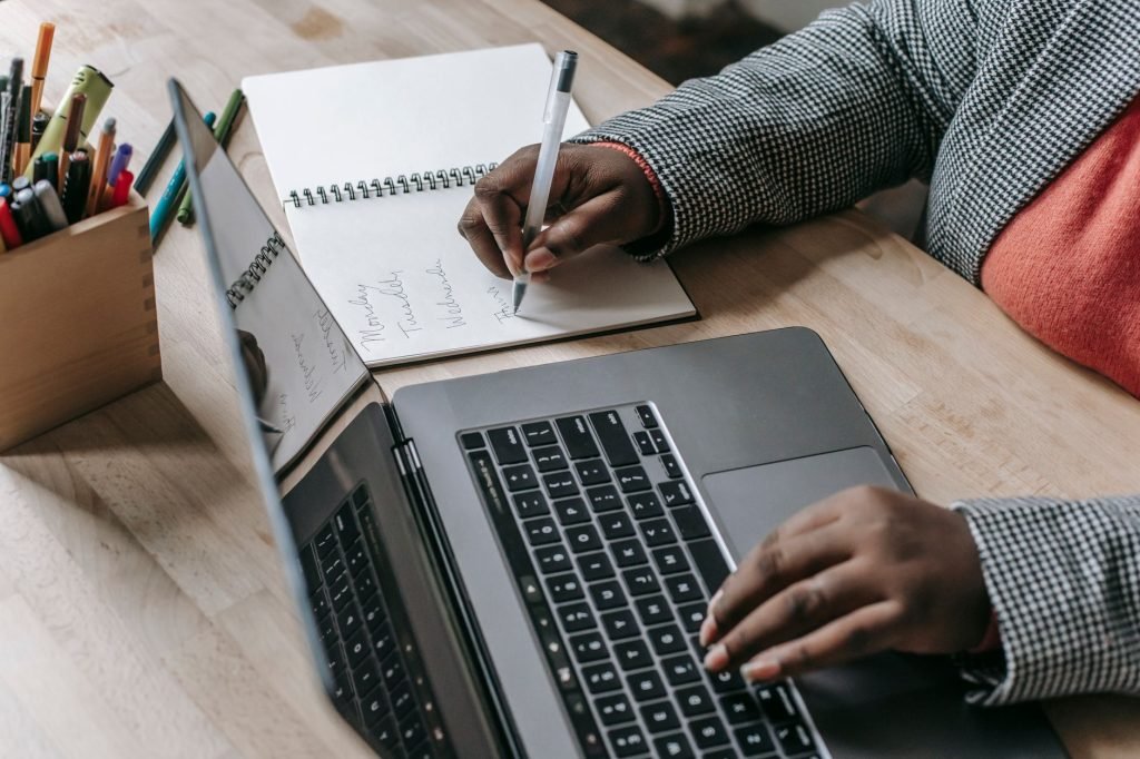 Crop unrecognizable African American female in formal wear writing notes in notepad while working on laptop — Sell Expanding