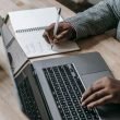 Crop unrecognizable African American female in formal wear writing notes in notepad while working on laptop — Sell Expanding