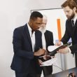 Three businessmen engaged in document signing in a modern office setting. — Take Profit Trader Allows You to Trade Without Us